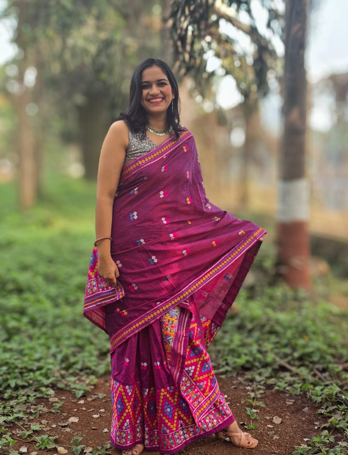 A woman posing in the Porgas Petal, a deep magenta handwoven Mishing Mekhela Chador with vibrant yellow and white Mirizim diamond motifs.