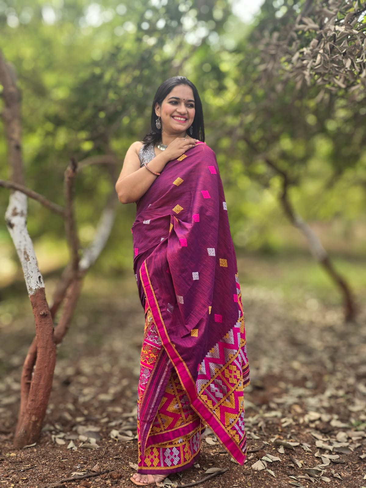 A woman smiling while draping The Dawn Ligang, a vibrant pink handwoven Mishing Mekhela Chador with intricate yellow and magenta geometric motifs.