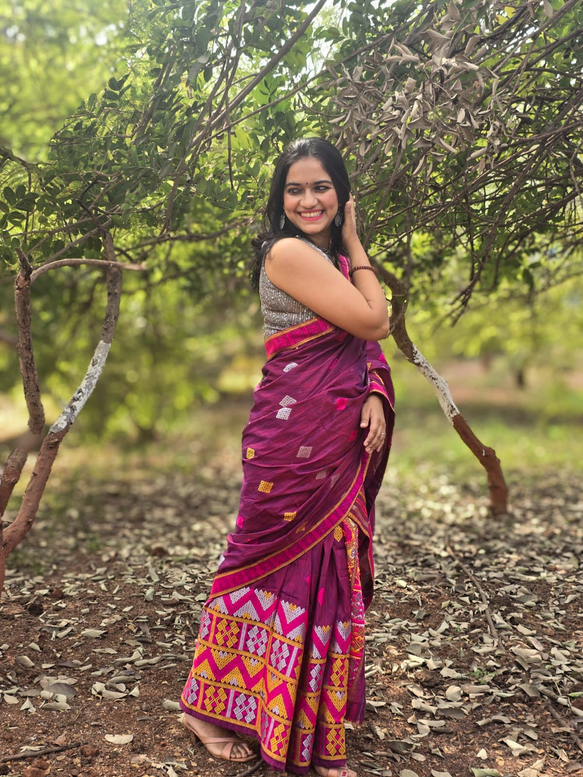 A woman smiling while draping The Dawn Ligang, a vibrant pink handwoven Mishing Mekhela Chador with intricate yellow and magenta geometric motifs.